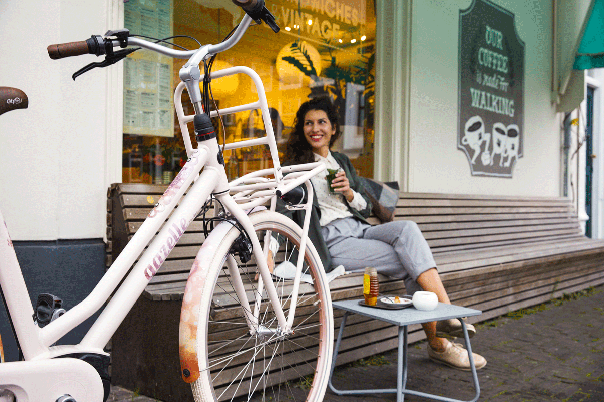 Gazelle Stadtrad vor einem Vintage Café, eine Person sitzt auf einer Holzbank und trinkt etwas